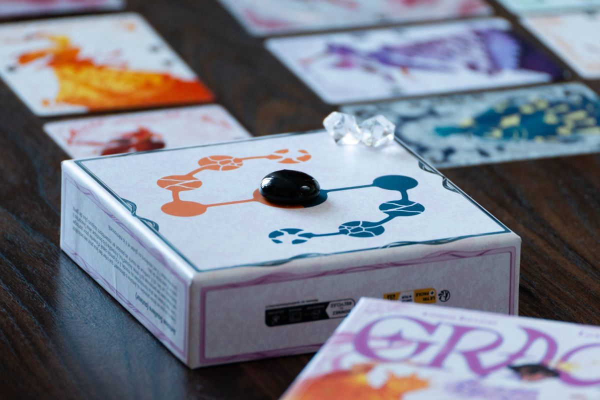 Une boîte de jeu posée sur une table en bois, entourée de cartes illustrées disposées en grille.