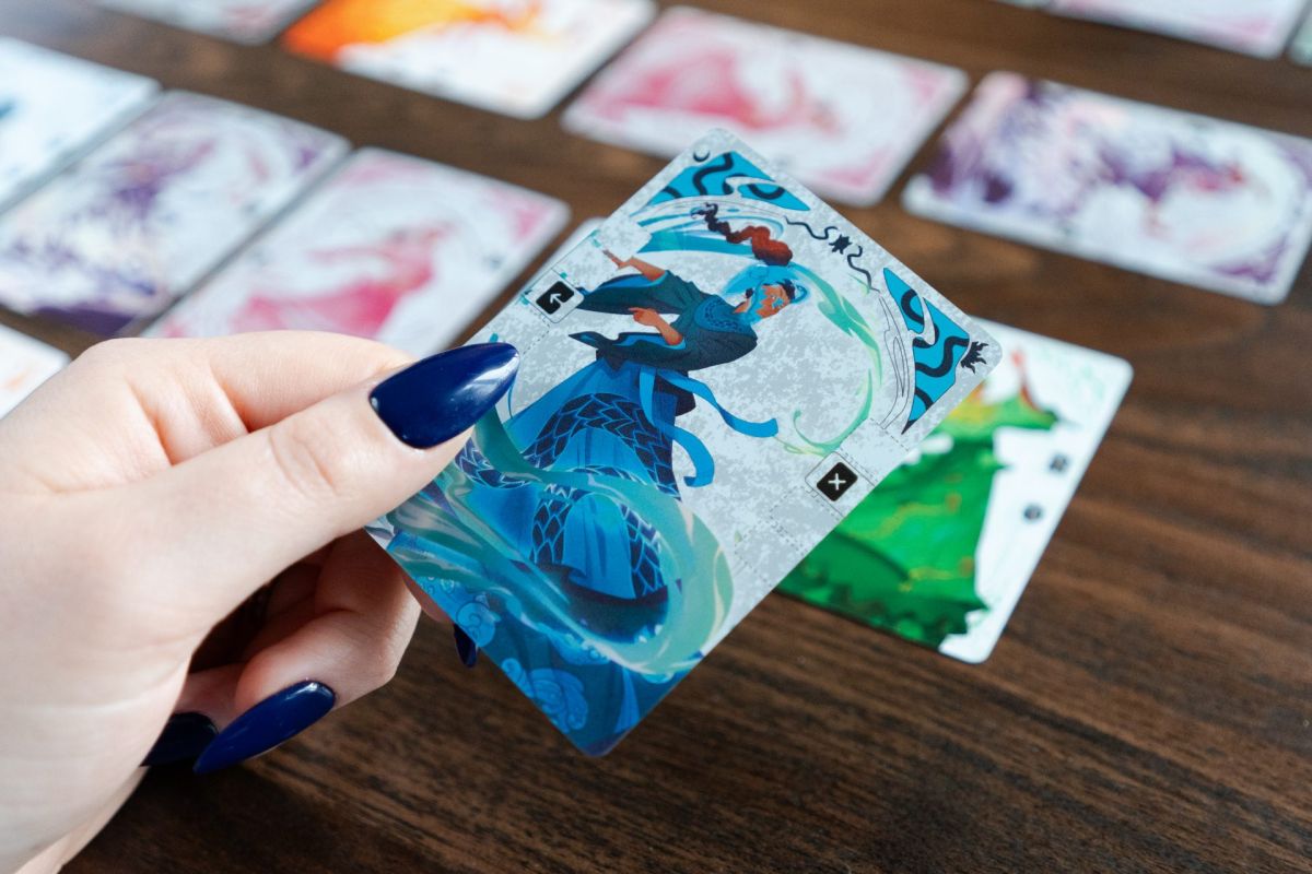 Une main tient une carte illustrée au-dessus d'une table où d'autres cartes sont étalées.
