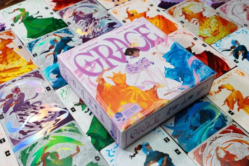 La boîte du jeu Grace posée au centre de ses cartes illustrées, étalées faces visibles.